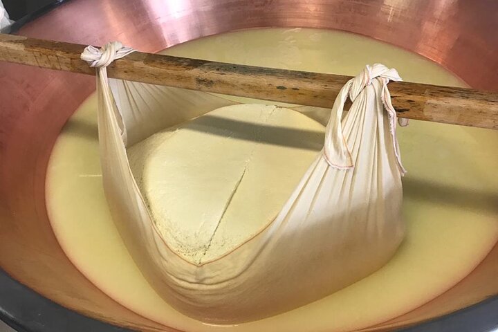 Fresh Parmigiano Reggiano curd wrapped in cloth inside a copper cheese vat during morning production